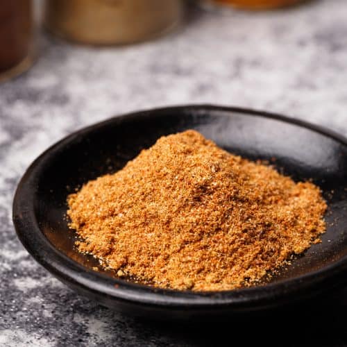 Shawarma spice mix in a black wooden dish next to spice jars.