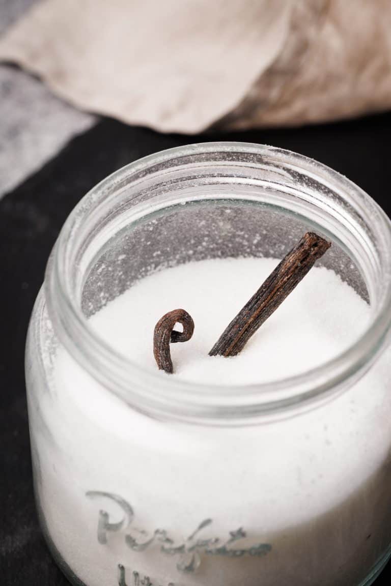 A mason jar filled with sugar with a vanilla bean sticking out.