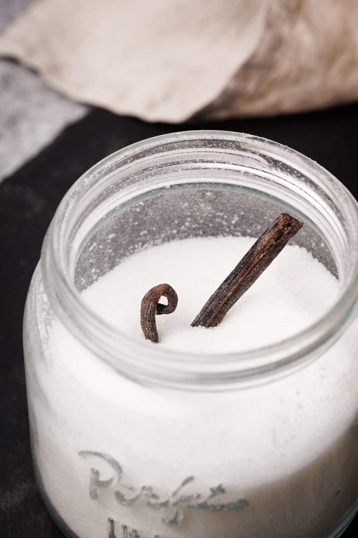 A mason jar filled with sugar with a vanilla bean sticking out.
