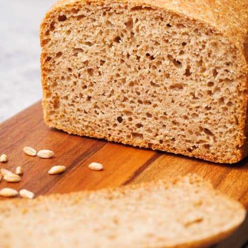A loaf of whole grain spelt bread on a wooden board.